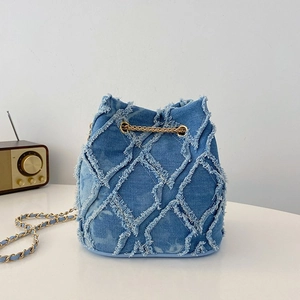 Detail of blue denim bucket bag featuring frayed quilted texture and gold chain strap