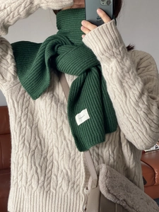 Close-up of green knit scarf featuring a soft texture and white brand label detail