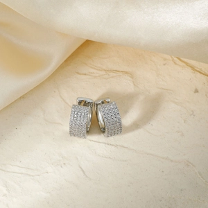 Créoles en argent avec zircons sertis sur fond de soie champagne et texture de pierre