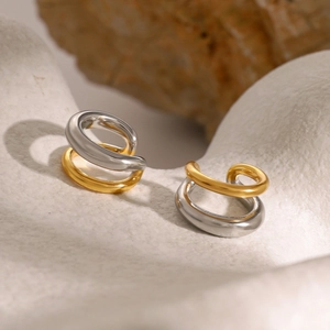 Macro shot of minimalist dual-tone gold and silver ear cuffs on a stone textured base