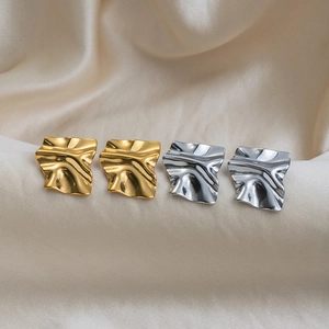 Detail view of 18K gold and silver pleated square earrings on beige silk fabric