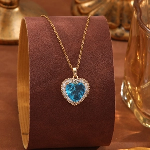 Detailansicht einer goldenen Herzkette mit blauem Kristall und funkelndem Rahmen