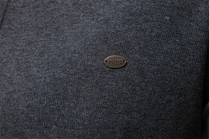 Detailed close-up of dark grey knitted fabric texture and a metal brand logo on a cardigan