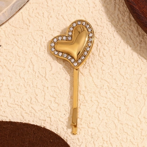 Close-up of gold plated heart hair clip with sparkling rhinestones on beige background