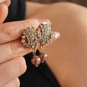 Vintage gold hollow pearl drop earrings with rhinestones held in a close-up hand view