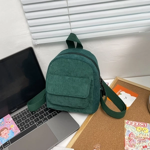 Detailed close-up of a green corduroy mini backpack on a wooden desk with a laptop