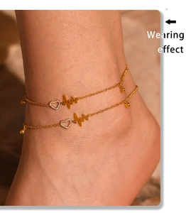 Detail of a gold double-layer anklet with heartbeat design and small heart pendant on ankle
