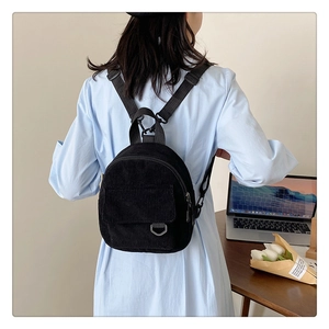 Detail view of mini black corduroy backpack with front pocket worn on casual outfit