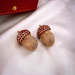 Close-up of acorn-shaped pendant with red and champagne crystals on white satin