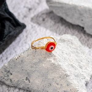 Macro view of a handmade gold wire-wrapped ring with a red evil eye bead on white stone