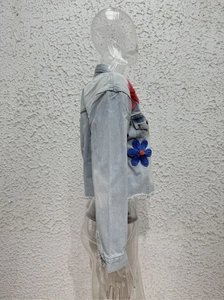 Detail of light blue denim jacket with red and blue knit floral patches and raw edge hem
