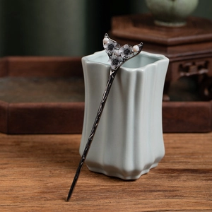Detail of a vintage Chinese hair pin with grey flowers and pearls on a ceramic vase