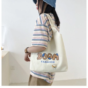 Detailansicht der großen Canvas-Schultertasche in Beige mit Cartoon-Bär und Aufdruck