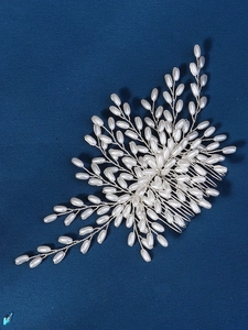 Detail of handmade pearl hair comb with silver wire leaf design on blue background