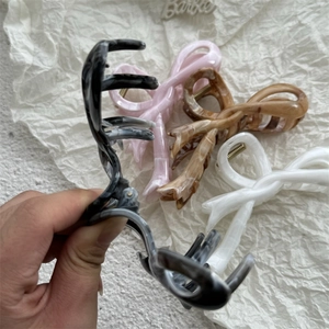 Detail of four butterfly bow-shaped claw clips in marble black, pink, amber, and white