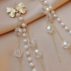 Elegant gold bow earrings with long pearl and crystal tassels on champagne silk backdrop