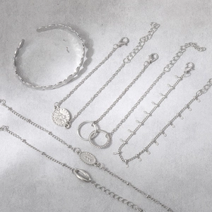 Detail of silver bohemian jewelry set with coin charms and open bangle on stone surface