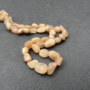 Close-up of irregular peach moonstone beads on a textured dark stone background