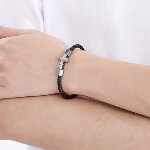 Macro view of black steel cable bracelet featuring a silver cross and square beads