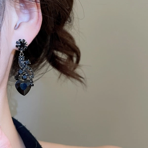 Close-up of elegant black heart and flower drop earrings worn by a model