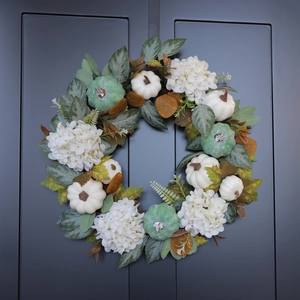 Fall wreath with white pumpkins, maple leaves and berries hanging on a dark grey door