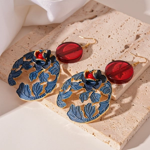 Detail of vintage style earrings with red resin disks and blue golden rose motifs