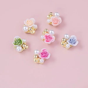 Flat lay of 3D resin rose nail charms with pearls and gold beads on pink background