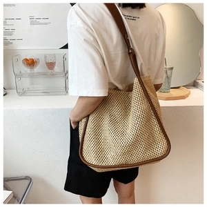 Detail of the woven straw tote bag featuring leather trim and brown shoulder straps
