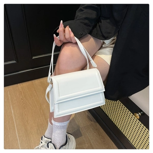 Detail shot of a minimalist white leather square bag with thin shoulder strap on a model