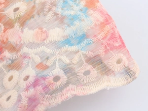 Macro-detail van tie-dye stof met gebroken witte borduursels en opengewerkte kanten randen