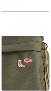 Detailed view of pink enamel cowboy boot and hat pins pinned on a green canvas bag