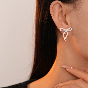 Close-up of a sweet white lacquered bow earring on a model for a minimalist fashion look
