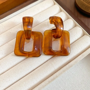 Macro shot of amber tortoiseshell resin square hoop earrings on a soft velvet display
