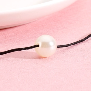 Minimalist double-layered necklace with cream pearl on black woven cord over pink surface