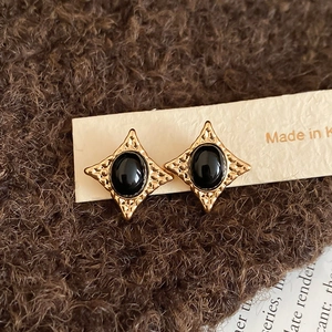 Macro shot of vintage gold earrings with textured diamond frame and oval black inlay