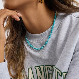 Detailed view of turquoise beaded necklace with gold accents worn by a model in casual wear