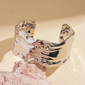 Detail shot of a silver textured wide open cuff bracelet on a rough stone pedestal