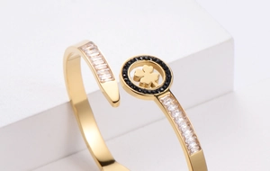 Dettaglio del bracciale a quadrifoglio dorato con zirconi pavé su supporto bianco
