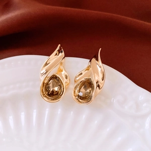 Macro detail of gold-tone vintage teardrop earrings with amber stones on white ceramic