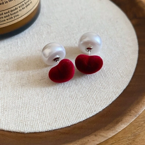 Detail of red flocked heart earring with pearl bead on a natural fabric background