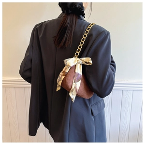 Detail of brown suede crescent bag with gold chain strap and ribbon bow accent