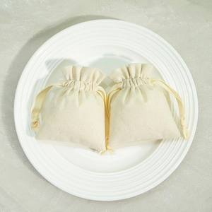 Two beige cotton drawstring jewelry bags displayed on a white ceramic plate with a grey desk