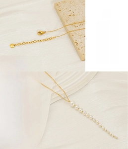 Détail du collier en acier doré avec des perles blanches graduées et un fermoir mousqueton
