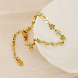 Detailed shot of golden stainless steel daisy bracelet draped over white ceramic decor