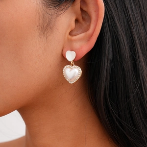 Macro detail of elegant heart-shaped earrings with pearls and crystals on a model