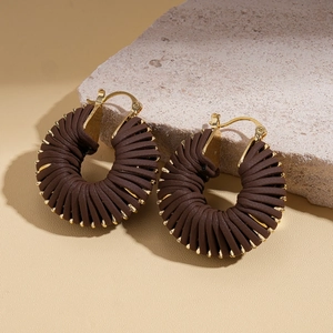 Detail of brown faux leather braided hoop earrings with gold accents on a stone