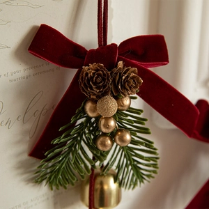 Christmas decoration featuring red velvet bow, pine cones, and golden bell on pine needles