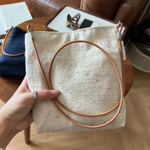 Detail of white cotton linen crossbody bag with rainbow neps and brown leather strap