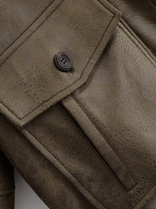 Detailed close-up of vintage leather texture and buttoned flap pocket on jacket