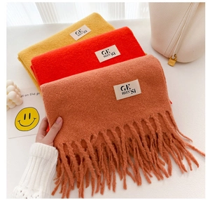 Detail of wool-like scarves in ginger, red, and orange with soft tassels and brand label